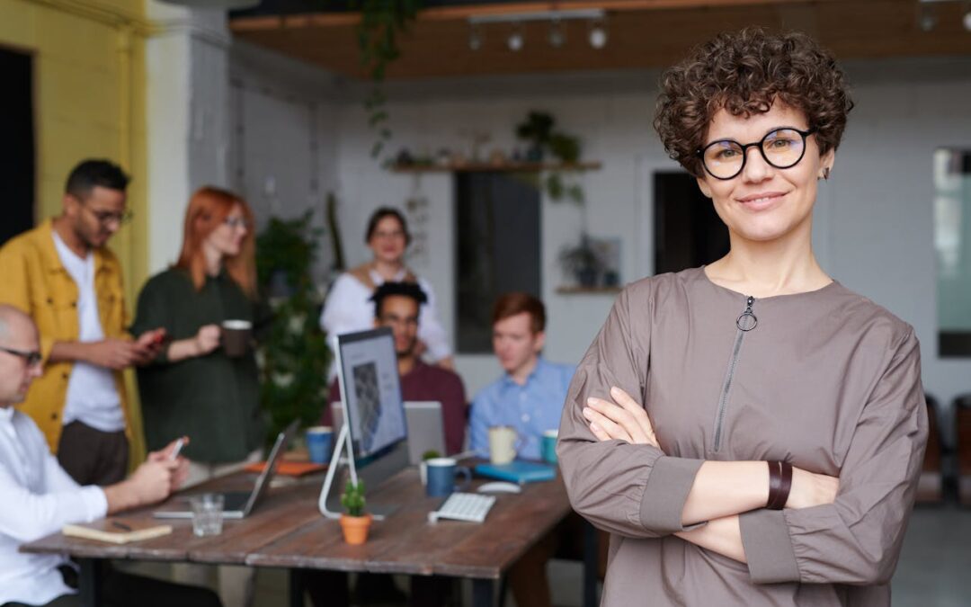 woman with arms crossed in foreground with team of employees in the background; self-awareness