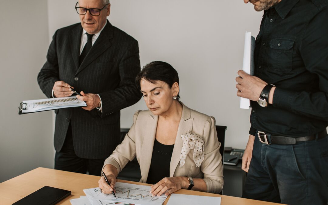 woman seated at desk with 2 men standing on either side of her; self-awareness